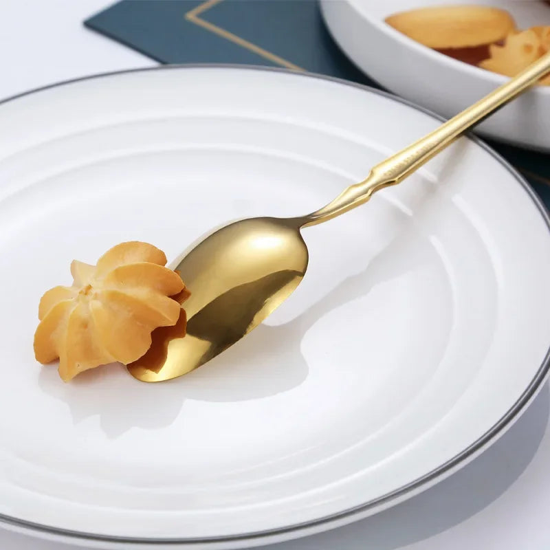 Stainless steel dinnerware set featuring a gold spoon with a pastry on a white plate.