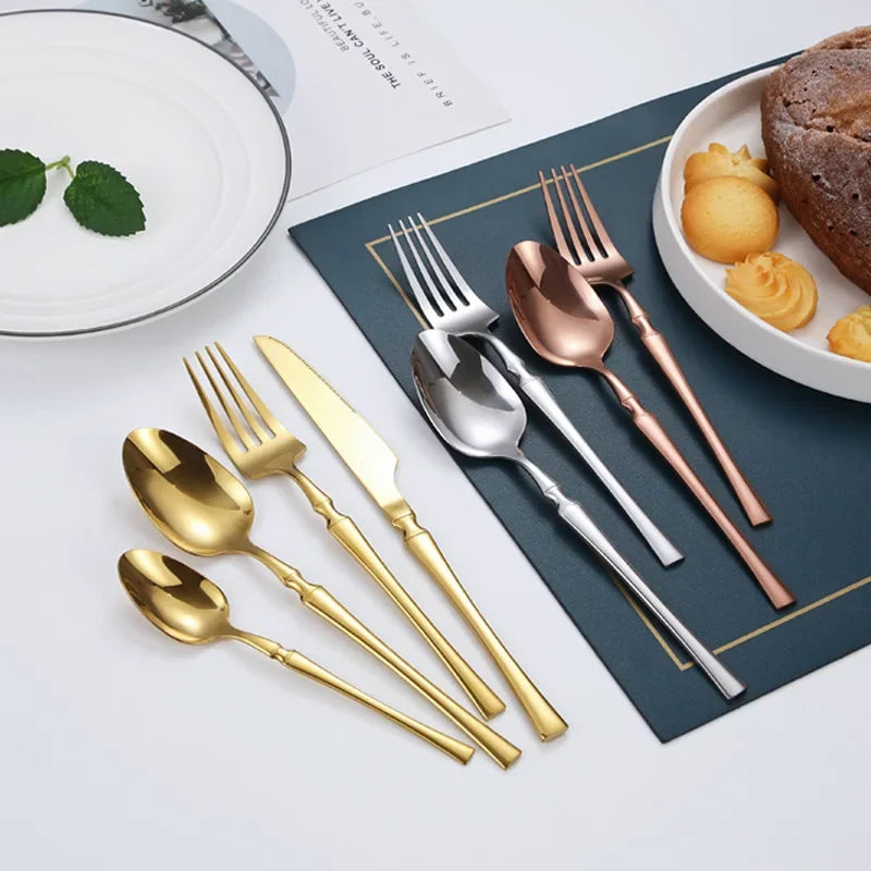 Stainless steel dinnerware set including gold and silver fork, knife, and spoon arranged next to dessert on table.
