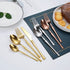 Stainless steel dinnerware set including gold and silver fork, knife, and spoon arranged next to dessert on table.